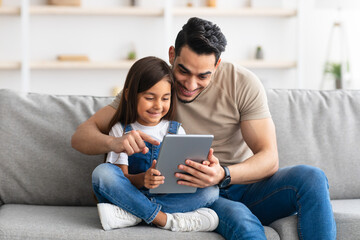 Smiling dad and daughter sitting on couch, using tablet