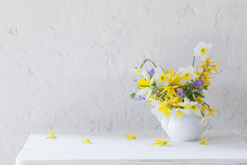 white and yellow spring flowers in vase on wooden table on white background