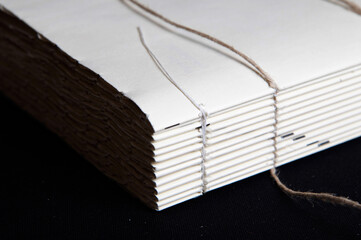The process of book binding; close up of a raw book after sewing on cords. Black background - obrazy, fototapety, plakaty