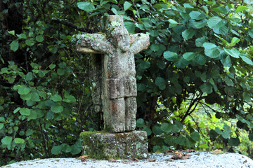 Traditional Galician stone cross, located in the middle of a forest. It shows a crucified Jesus, disfigured by the passage of time and half-covered with lichen.