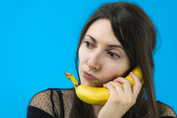 Giovane e bella ragazza si diverte telefonando con una banana su sfondo blu