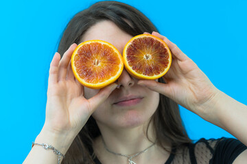 Una giovane e bella ragazza si diverte usando un arancia rossa tagliata a metà come occhi su sfondo blu
