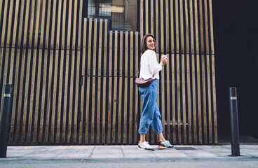 Happy woman in trendy wear with coffee walking on street