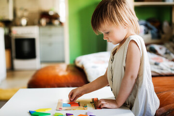 Cute caucasian child toddler playing with a wooden mosaic on the table, earlier child development and children's games, kid playing with a puzzle close-up, toning