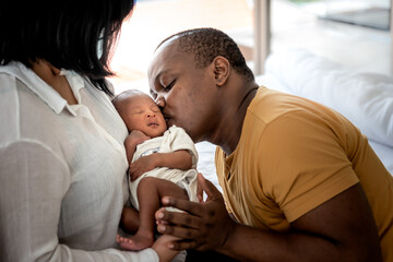 An African American father kissing face, his 12-day-old baby black skin newborn which mother was holding and sitting on bed, with love and happy, concept to African  family and baby black skin newborn