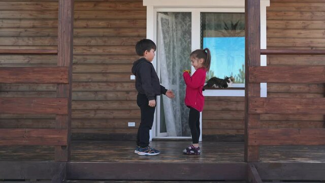 The boy gives the girl flowers and in return she kisses him Small children play on the terrace near a beautiful house Brother and sister love each other Happy family Funny kids
