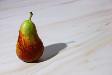 A green-and-red pear on a pink marble countertop casts a shadow to the right. Plenty of room for text.