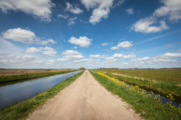 Fototapeta na wymiar Dutch landscape with a small road / cycling path, along a canal with blue sky and clouds, province Groningen, the Netherlands