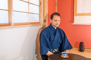 Traditional japanese house machiya ryokan with man in kimono by alcove and hanging paper scroll drinking green tea