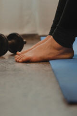 Vertical shot and close-up of the natural feet of a Latin woman. Leaning on a yoga mat with a dumbbell at hers side.