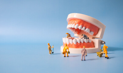 miniature workers clean and correct the tooth model on a blue background. Dental examination concept.Regular oral health is vital to oral health. - obrazy, fototapety, plakaty