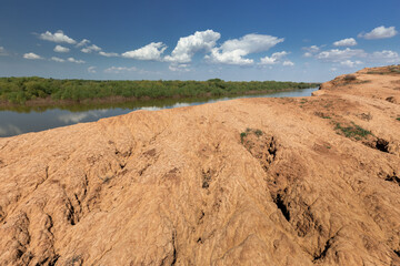 Landscape of a large river with a low forested bank in the background and a high desert bank of rugged sandstone in the foreground