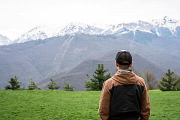 Fototapeta na wymiar young man in cap from behind looking view of snow capped peak Caucasus mountains, travel, mountain landscape, beauty in nature