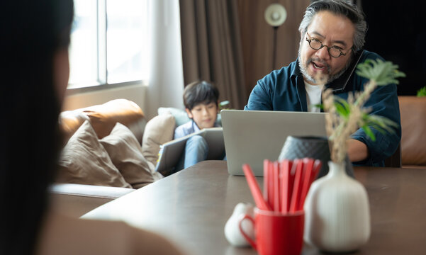 Asian Middle Aged Man Sitting At Home Working With Family At Home. Work From Home Concept