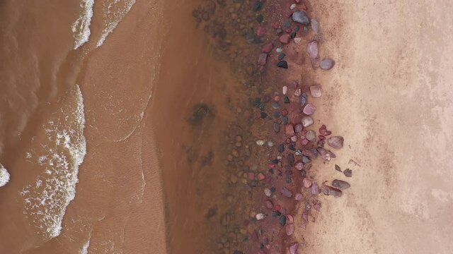 Aerial top down view of calm ocean waves crashing into beach at day
