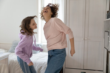 Joyful young teen kid daughter dancing to disco music in own room with happy mother, spending...