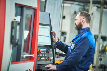 Industrial worker operating cnc machine at metal machining industry - obrazy, fototapety, plakaty