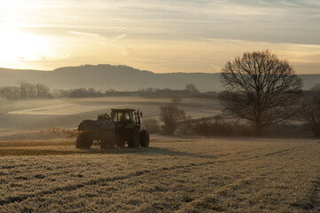 Closeup shot of a tractor driving early in the morning with hoarfrost liquid manure