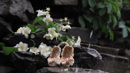 A bouquet of jasmine lies on the stones in the rain. Decorative bast shoes on the background of jasmine. Rainy day.