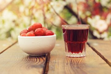 A bowl with cherry berries and a glass of cherry alcohol on the background of a flowering tree.