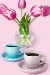 Fototapeta na wymiar Two cups of coffee and a vase with pink tulips on the pink background. Copy space. Close-up.
