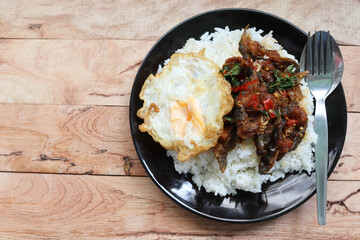 Rice, stir-fried basil catfish, egg, with spoon and fork in the dish isolated on wooden background closeup.
