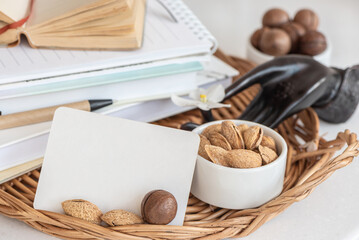 A stack of books and notebooks, a white blank card, a snack of nuts on a table in a wicker tray. Template for your text, copy space.