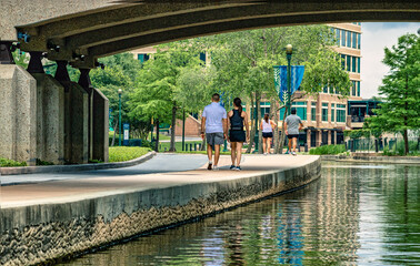 people walking along side the water under a bridge