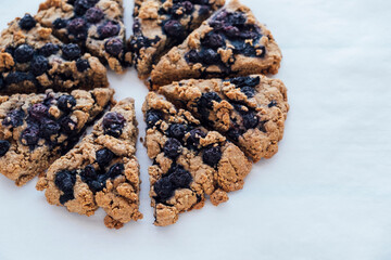 Freshly baked oat blueberry scones on baking paper on white wooden background, close up. Sweet food with natural ingredients. Vegan gluten free pastry.