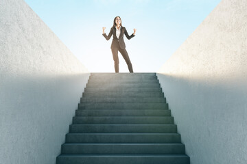 Ambition concept with joyful businesswoman in black suit on top of stairway on blue sky background.
