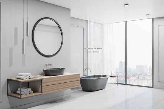 Modern spacious bathroom with city view from bug window, glossy floor, black bath and round mirror over black sink