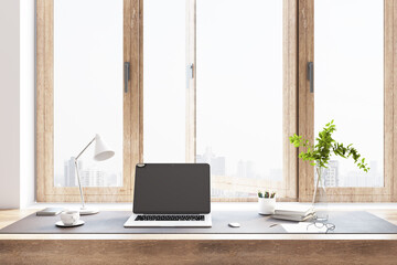 Sunny eco style home office work place with wooden details, laptop on tabletop and city view from huge window.