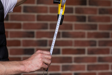 Man's hands holding length centimetre ruler for building use against red brick wall. Copy space. Focus is at the ruler. Building concept.