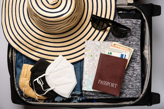 Open travel bag with summer clothes, hat, film camera and passports on white background, top view, flat lay
