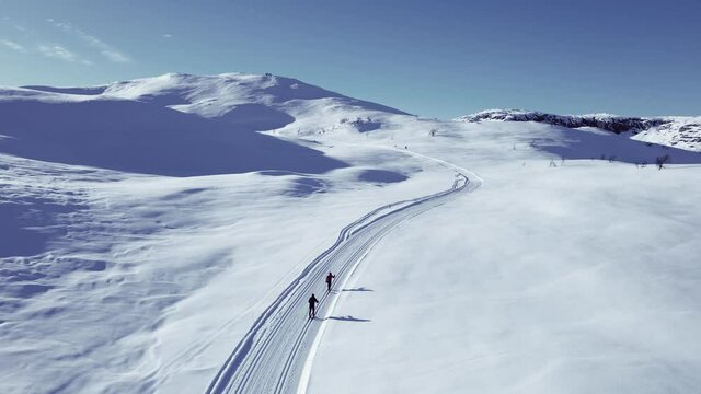 Active couple cross country skiing on a slope through wild snowy mountain wilderness on a clear cold winters day.