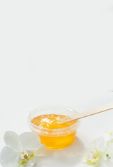 Sugar paste or wax honey in a transparent jar and white orchid on a white background. Sugaring. Depilation and beauty concept. Waxing.