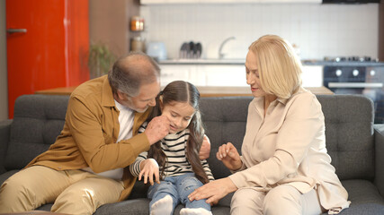 Grandfather and grandmother trying to make their sad little grandson laugh. They tickle their...
