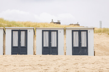 Picturesque coastal scenery with row of small closed square summer cubicle homes on Dutch North sea beach with dune behind on an overcast day