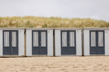 Row of simple small closed square summer cubicle homes on Dutch North sea beach with dune behind on an overcast day