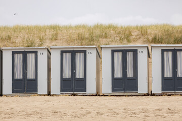 Small closed square summer cubicle homes on Dutch North sea beach with dune behind on an overcast day