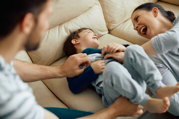 Joyful parents tickling their son and enjoying in family time at home.