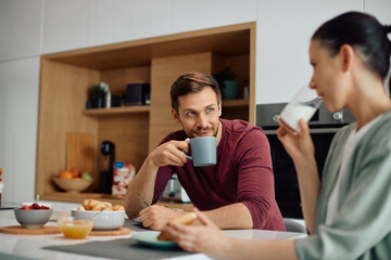 Smiling couple talking while eating breakfast together at dining table.