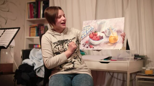 An artist blogger gives knowledge using the Internet. A teenage girl shows a picture in her hands. She talks about the motivation to paint.