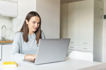 Work from home concept. Focused young woman using laptop computer for working from home, female freelancer works online sitting in the kitchen home, student learning on the distance