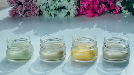 Four jars of cosmetic cream of different colors with a flowers background.