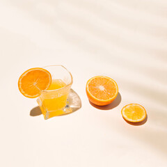 Summer tropical composition with yellow orange juices in a glass on the table with a shade of tropical leaves.