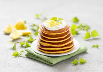 Breakfast lemon pancakes with cream on a plate on a light gray background