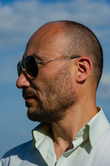 Fototapeta premium man in dark sunglasses looks to the side, portrait against a blue sky. Forty years old.