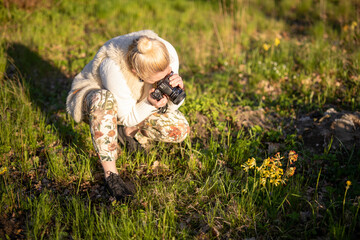 young woman photographs flowers in the meadow, spending free time, relaxing in the bosom of nature, amateur photography