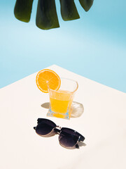 Summer tropical composition with yellow orange juice and sunglasses with the shadow of a monster leaf sticking out.